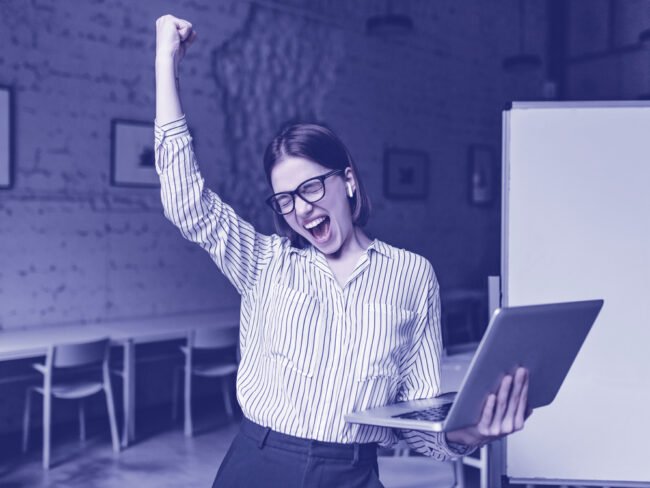 Business woman with laptop in hand is happy with success. Portrait of woman in glasses and striped blouse enthusiastically screaming and making winning gesture. ikigai
